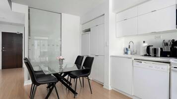 A modern kitchen with white cabinetry, a glass dining table with black chairs, and a dishwasher.