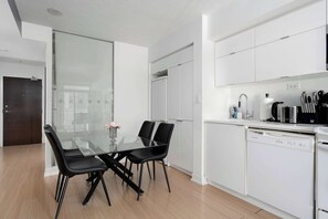 Une cuisine moderne avec des meubles blancs, une table à manger en verre et des chaises noires, ainsi qu’un lave-vaisselle.