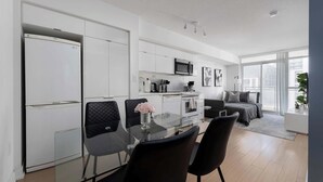 A modern kitchen with white cabinetry, a microwave, and a dining area with a glass table and black chairs. - Walk to Rogers Centre, CN Tower, Waterfront! (Toronto)