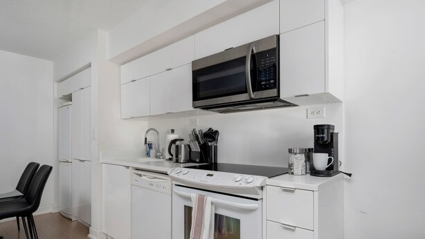 A modern kitchen with white cabinetry, a microwave, a coffee maker, and a dishwasher. - Walk to Rogers Centre, CN Tower, Waterfront! (Toronto)