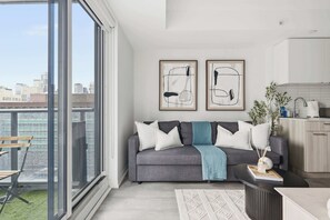 A modern living room with a grey sofa, white and blue throw pillows, and abstract artwork on the wall. - Radiant 2BR Downtown Retreat | Balcony & Views | Parking Available (Toronto)