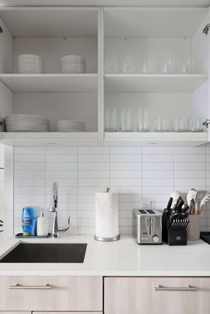 Een keuken met witte kasten, een spoelbak, een broodrooster en een bestekhouder.