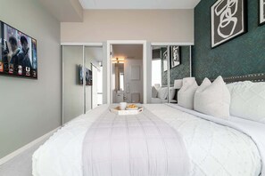 A bedroom with a large bed, a bedside table, a mirror, and a wall with framed artwork. - City Lights & Skyline Nights, Bay Street Penthouse (Toronto)