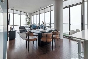 A modern interior with a round dining table surrounded by six chairs, a sofa, and a large window providing a view. - City Lights & Skyline Nights, Bay Street Penthouse (Toronto)