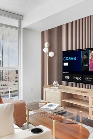 A modern living room with a large flat-screen TV displaying the 'CRAVE' logo, a wooden slatted wall, a glass coffee table, and a sofa. - Sleek 2BR Waterfront Condo Perfect City Getaway | Parking Available (Toronto)