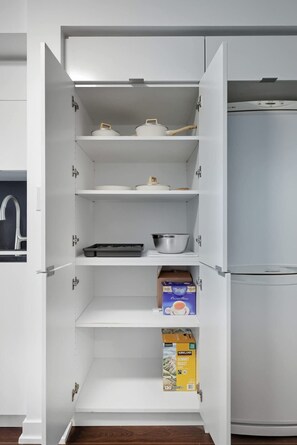 A white kitchen with a built-in refrigerator, a sink, and shelves with kitchenware.