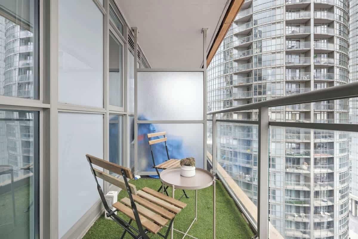 A balcony with a small table and two chairs, a potted plant, and a view of a high-rise building.