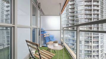 A balcony with a small table and two chairs, a potted plant, and a view of a high-rise building.