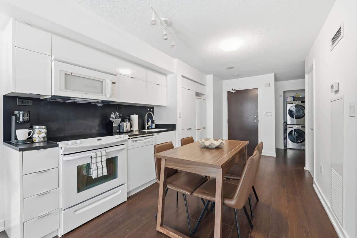 A modern kitchen with white cabinetry, a built-in oven, and a dining table with chairs.
