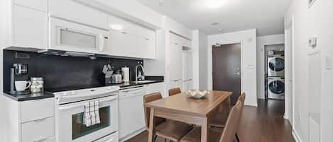 Cozinha moderna com armários brancos, forno embutido e mesa de jantar com cadeiras.