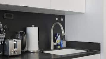A compact kitchen with a black countertop, white cabinets, a stainless steel sink, and a dishwasher.