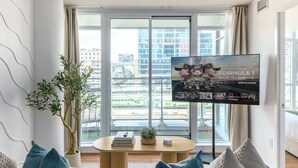 Uma sala de estar moderna com uma janela ampla, uma televisão de tela plana, um sofá e uma mesa de centro.