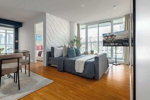 A modern living room with a sofa, a glass coffee table, and a television. - Expansive 3BR Downtown Condo with Patio (Toronto)