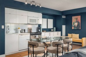 A modern kitchen with white cabinets, a glass dining table, and a sofa in a room with blue walls. - Expansive 3BR Downtown Condo with Patio | Parking Available (Toronto)