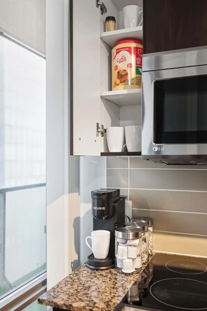 Une petite cuisine équipée d’une machine à café, d’un four à micro-ondes et d’une étagère sur laquelle se trouve une boîte de café.