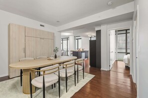 A modern dining area with a wooden table and chairs, a kitchen in the background, and a view through an open door. - Designer Bay Street Condo Sleep 6 (Toronto)