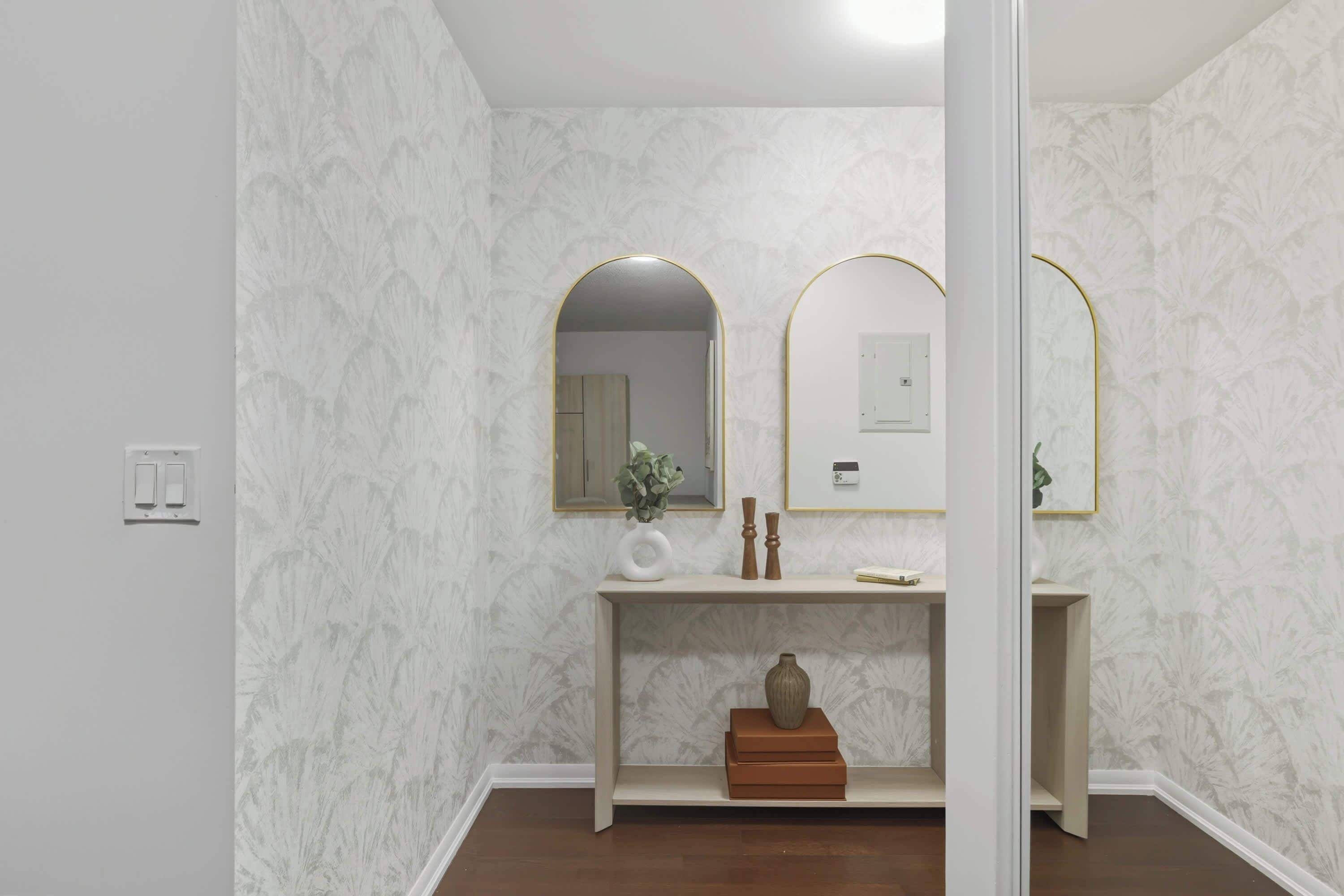A bathroom with a marble wall, a wooden vanity, a mirror with a gold frame, and a light switch.