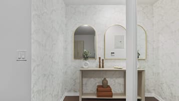 A bathroom with a marble wall, a wooden vanity, a mirror with a gold frame, and a light switch.