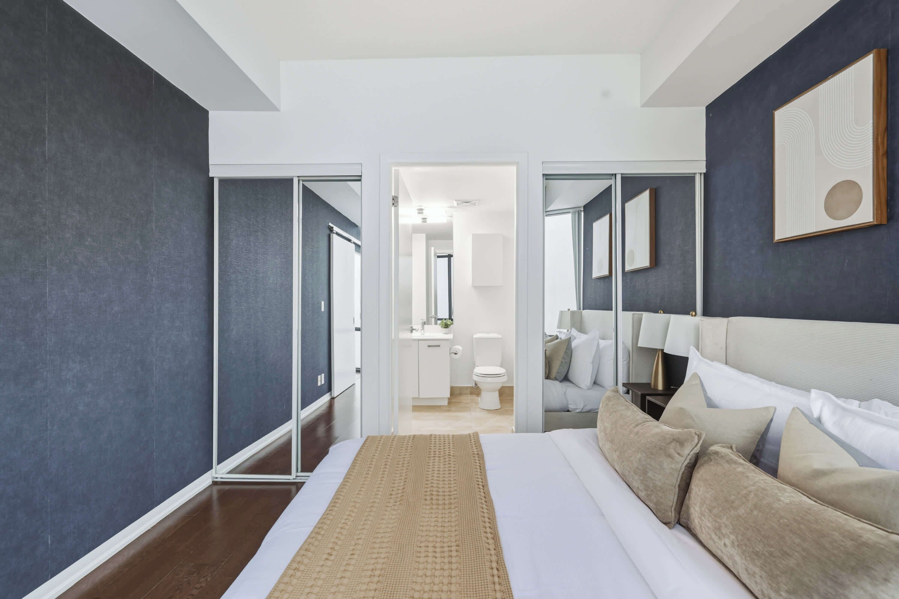 Un dormitorio moderno con una cama grande, una mesita de noche, un espejo y vistas al baño.