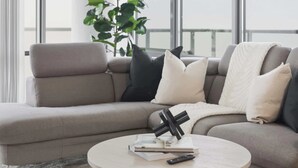 En moderne stue med en grå sofa, et rundt sofabord og et stort vindue der giver udsigt til himlen.