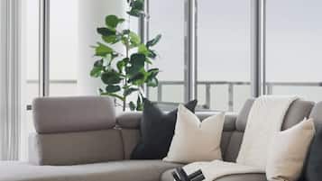 A modern living room with a grey sofa, a round coffee table, and a large window providing a view of the sky.