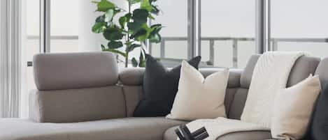 Una sala de estar moderna con un sofá gris, una mesa de centro redonda y un gran ventanal con vistas al cielo.