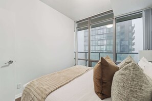 A hotel room with a large window, a bed with a white and beige blanket, and two pillows. - Designer Bay Street Condo Sleep 6 (Toronto)