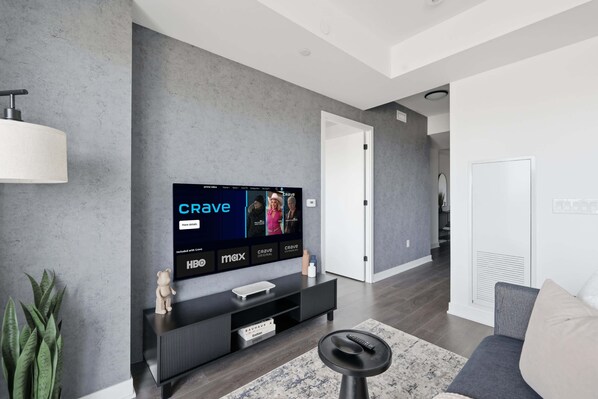 Un salon moderne avec un téléviseur à écran plat fixé à un mur gris, un meuble de rangement noir en dessous et un canapé gris agrémenté d’un tapis à motifs.