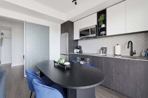 Une cuisine moderne dotée d’un îlot central, de meubles de couleur sombre et d’un dosseret en carreaux disposés en motif chevron.