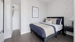 A bedroom with a bed, a nightstand, a wall-mounted picture, and a door leading to a bathroom.