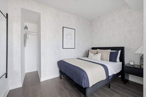 Une chambre à coucher comprenant un lit, une table de chevet, un tableau accroché au mur et une porte donnant sur une salle de bain.