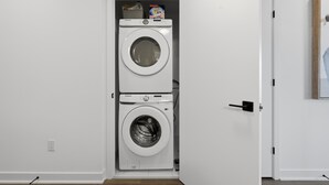 A compact laundry room with two stacked washing machines, a door with a handle, and a wall socket.