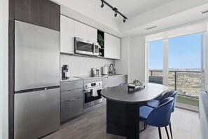 A modern kitchen with a built-in microwave, oven, and refrigerator. There is a dining area with a table and chairs. - Chic 2BR Retreat | Parking Available (Toronto)