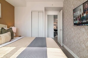 A hotel room with a bed, a TV mounted on the wall, and a door leading to a bathroom. - Chic Downtown 3BR Retreat Private Patio (Toronto)