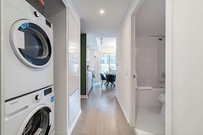 A laundry room with a washing machine and dryer, a dining area with a table and chairs, and a shower area with a bathtub and toilet. - Chic Downtown 3BR Retreat Private Patio (Toronto)