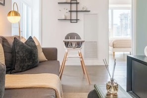 A modern living room with a sofa, a high chair, a lamp, and a small table with a bottle.