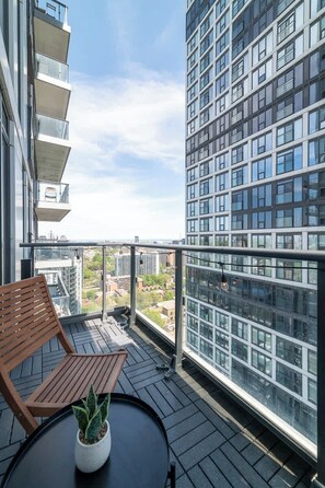 A balcony with a wooden chair and a potted plant, overlooking a cityscape with modern buildings. - Chic Downtown 3BR Retreat Private Patio (Toronto)