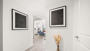 A hallway with two framed abstract artworks on the walls, a vase with dried flowers on the floor, and a glimpse of a modern kitchen and living area in the background. - City Living Downtown Retreat Perfect Getaway! (Toronto)