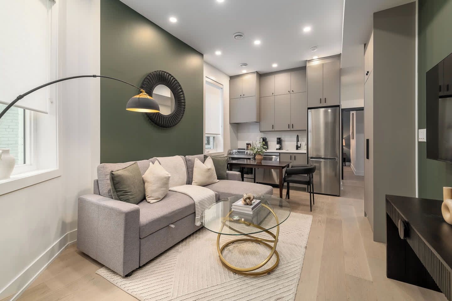 A modern living room with a grey sofa, a glass coffee table, and a ring light on the wall.
