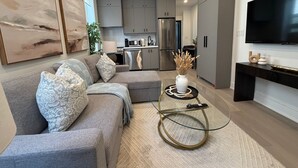 A modern living room with a grey sofa, a coffee table, and a flat-screen TV. - Parkdale 2-Bedroom Apartment Free Parking (Toronto)