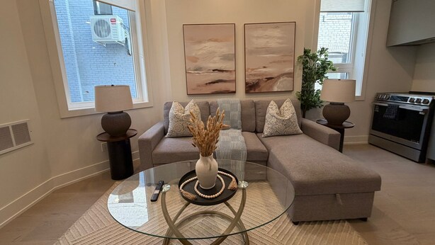 A living room with a glass coffee table, beige sofa, and artwork on the wall. - Parkdale 2-Bedroom Apartment Free Parking (Toronto)