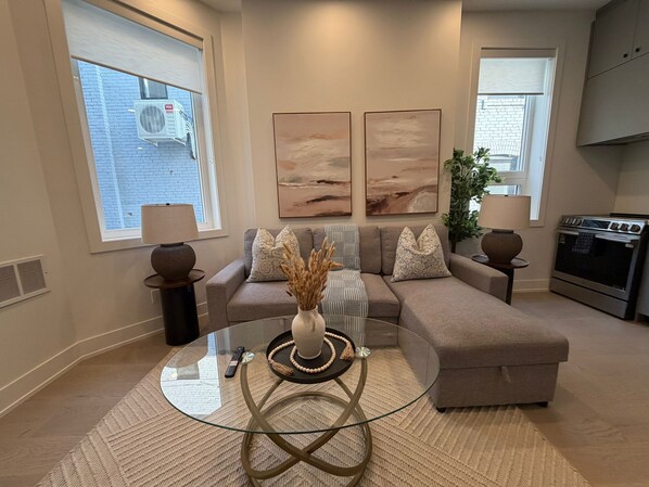 A living room with a glass coffee table, beige sofa, and artwork on the wall.