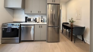 A modern kitchen with stainless steel appliances, grey cabinetry, and a dining area with a table and chairs. - Parkdale 2-Bedroom Apartment Free Parking (Toronto)