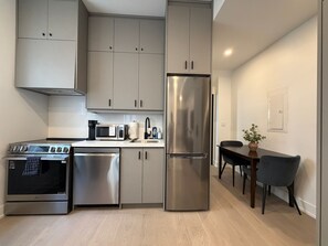 A modern kitchen with stainless steel appliances, grey cabinetry, and a dining area with a table and chairs.