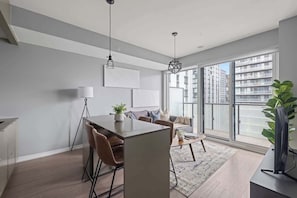 A modern living room with a dining area, large windows, and a view of the city. - Stunning 1BR Suite, Private Balcony & City Views | Parking Available (Toronto)