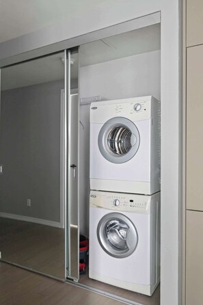A compact laundry room with two stacked washing machines, a sliding door, and a tiled floor. - Stunning 1BR Suite, Private Balcony & City Views | Parking Available (Toronto)