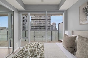 A bedroom with a large bed, a balcony with a city view, and a sliding glass door leading to an outdoor area. - Stunning 1BR Suite, Private Balcony & City Views | Parking Available (Toronto)