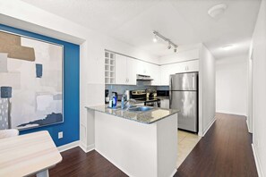 A modern kitchen with white cabinets, a stainless steel refrigerator, and a granite countertop. - Free Parking! Huge 3BR CityPlace Condo | Parking Available (Toronto)