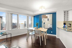 Een moderne keuken met een blauwe accentmuur, een eethoek met tafel en stoelen en grote ramen met uitzicht op de stad.