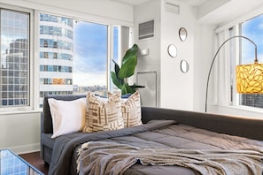A modern bedroom with a large bed, city views, and a plant. - Free Parking! Huge 3BR CityPlace Condo | Parking Available (Toronto)